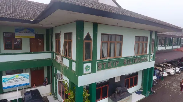 Pandangan udara gedung A di STKIP Siliwangi, memiliki banyak jendela dan mobil yang terparkir di depannya. Gedung tersebut juga memiliki logo "STKIP SILIWANGI" dan plang "PASCASARJANA" di bagian depan.